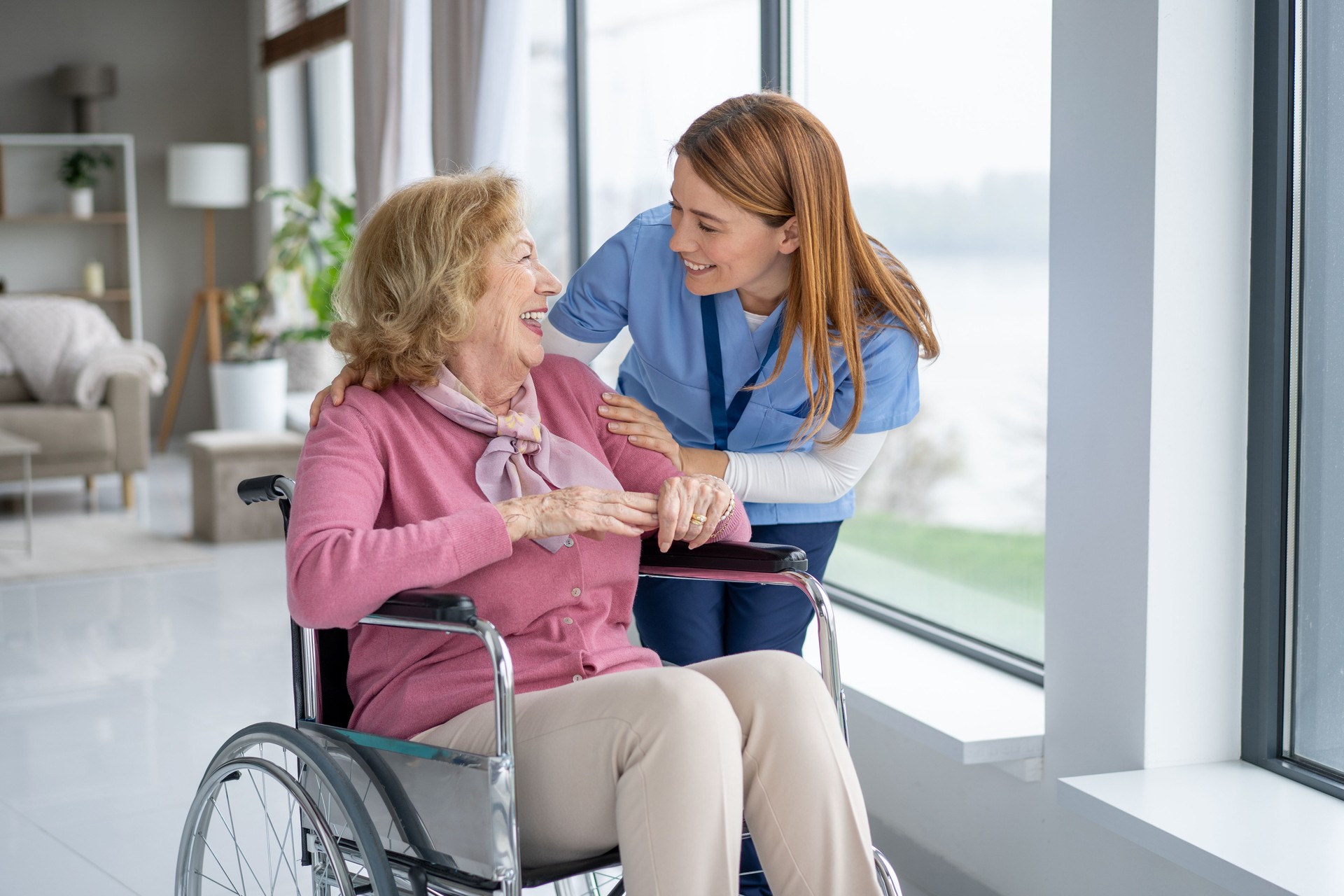 Nurse assisting elderly woman smiling by the window
